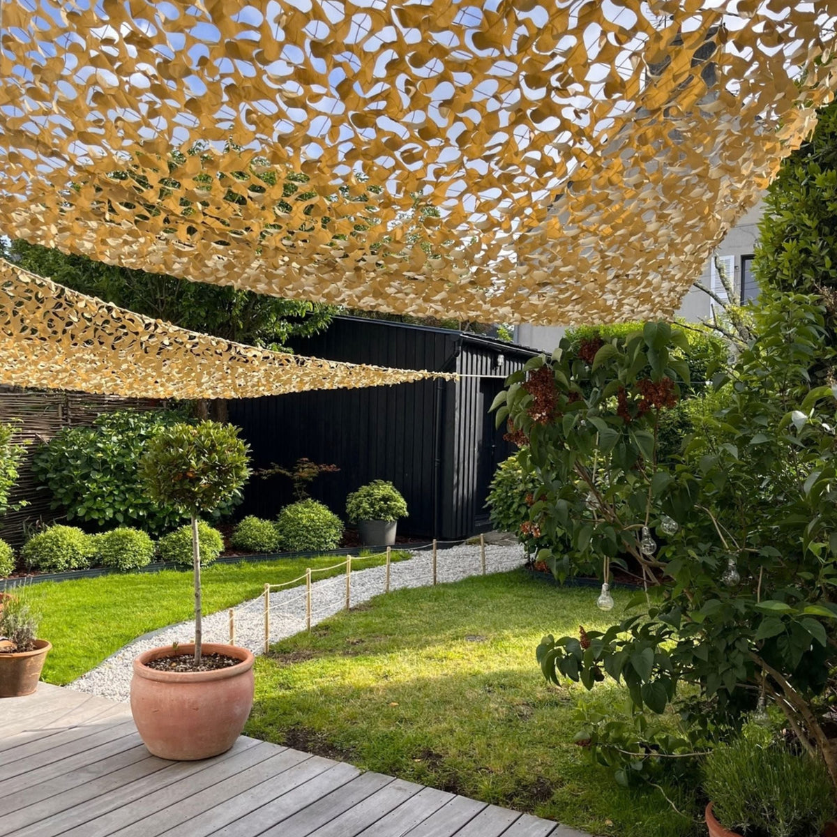 Reti mimetiche triangolari beige come teli ombreggianti in un giardino